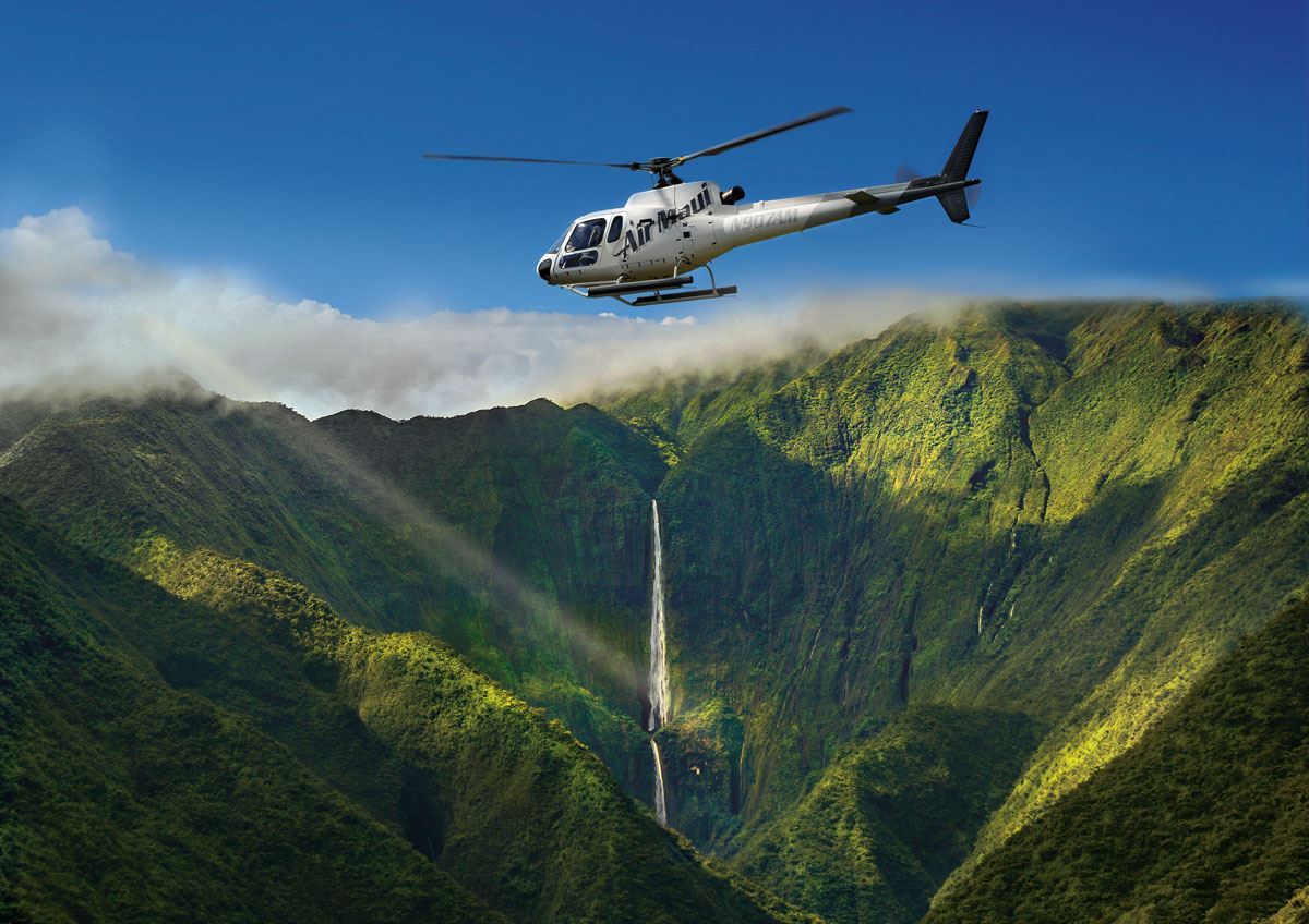 Helicopter flying over lush green mountains with a waterfall cascading in the background.