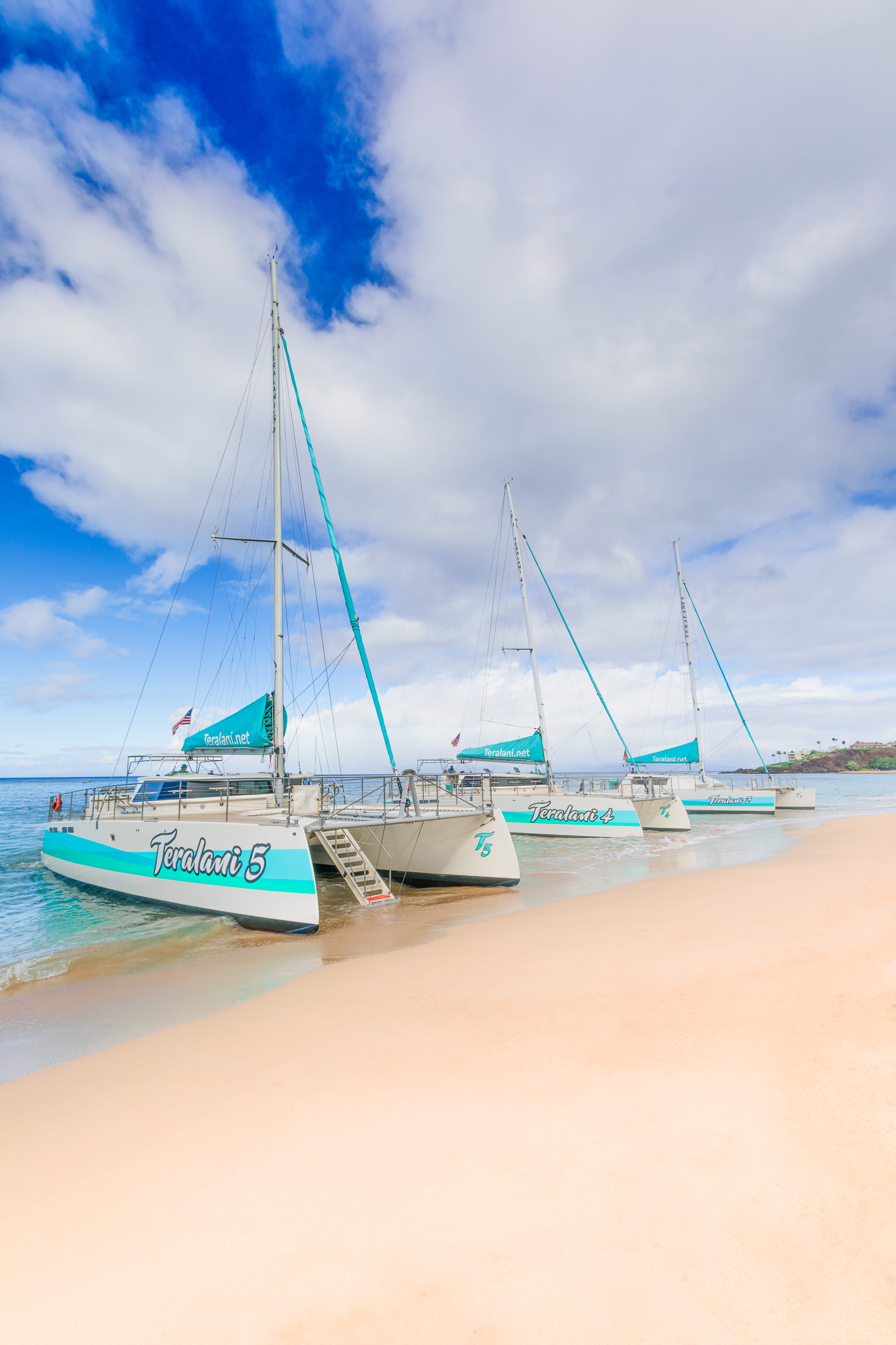 Three catamarans on a sandy beach under a cloudy sky.